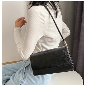 Detail of black crocodile pattern baguette bag showing golden metal buckle and shoulder strap