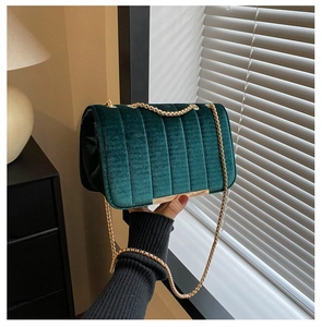 Detail of dark green velvet crossbody bag with gold chain and vertical quilted texture