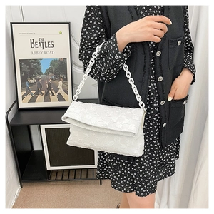 Detail of white quilted crossbody bag featuring a chunky plastic chain strap on a model