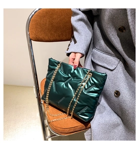 Detail of dark green quilted tote bag with glossy finish and gold chain strap on chair