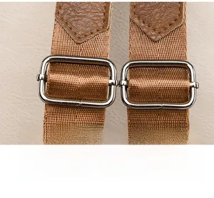 Close-up of adjustable woven shoulder strap and silver metal buckle on brown backpack