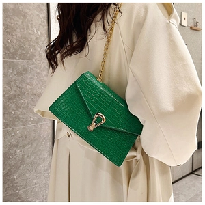 Close-up of green crocodile embossed square bag with golden horseshoe lock on trench coat