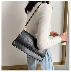 Detail of black crocodile embossed handbag worn under arm with golden metal hardware
