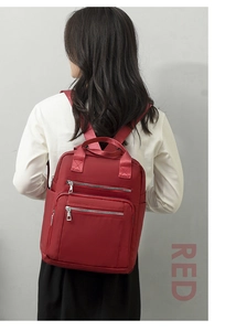 Rear view of a model wearing a red nylon backpack with multiple metallic zippers