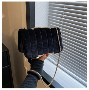 Detail view of black velvet chain bag with vertical quilting and gold metal hardware