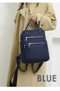 Detail of navy blue nylon quilted backpack with silver zippers worn with a trench coat