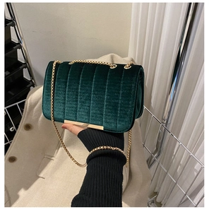 Detailed close-up of dark green velvet shoulder bag with gold chain and quilted texture