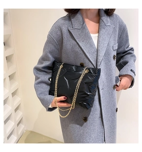 Detail of black quilted puffer tote bag with gold chain strap on grey wool coat