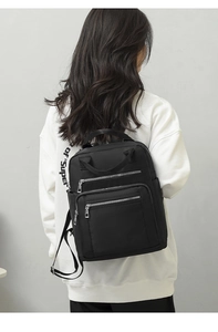 Detailed back view of a minimalist black quilted nylon backpack worn by a female model