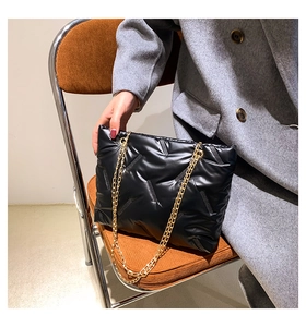 Detail of black quilted puffer bag with gold chain straps on a gray wool coat