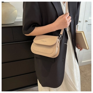 Dettaglio della borsa a tracolla beige con motivo a coccodrillo e logo su una modella