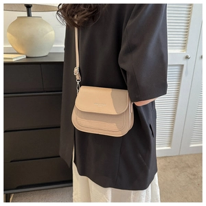 Dettaglio borsa a sella beige con trama coccodrillo e patta magnetica su modella