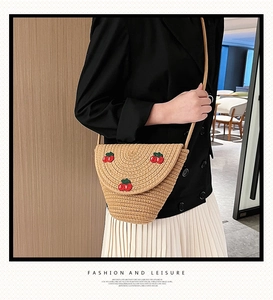 Detailed view of woven straw crossbody bag with red cherry embroidery worn by a model