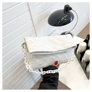 Detail view of a white quilted crossbody bag with a thick chain strap in a modern setting