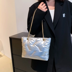 Silver quilted metallic tote bag with golden chain straps worn on a black blazer