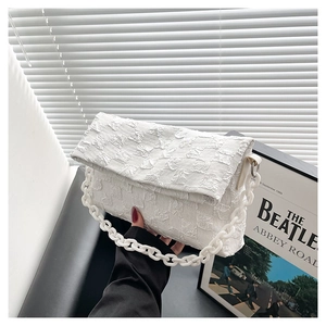 Close-up of white quilted crossbody bag with chunky acrylic chain in minimalist setup