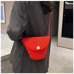 Detailed texture of red woven shoulder bag with large white pearl closure on grey suit