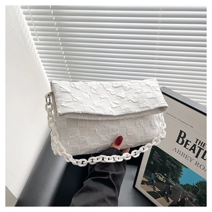 Detail of white textured lattice crossbody bag with bold decorative plastic chain