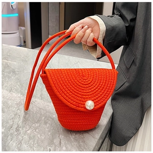 Detail of orange woven straw bag featuring spiral texture and a large pearl closure