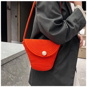Detail of orange woven straw bag featuring a pearl button and spiral texture shoulder strap