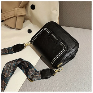 Dettaglio della borsa a tracolla nera con cuciture a contrasto e tracolla in jacquard