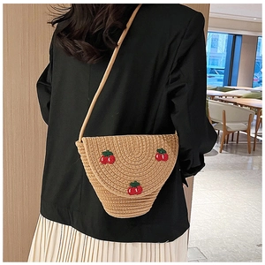 Detail of hand-woven straw bag featuring red cherry embroidery and cotton rope strap