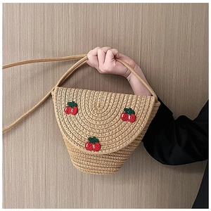 Detail of straw woven crossbody bag featuring three red cherry appliques and thin rope strap