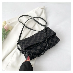 Detail of black checkerboard texture on crossbody bag with chunky chain and leather strap