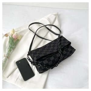 Detail view of black checkered chain bag with textured fabric on a white blazer background