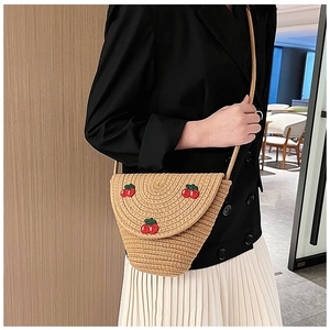 Detail of hand-woven straw crossbody bag featuring three red cherry embroidery patterns