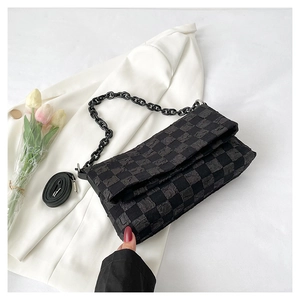 Detail of black checkered crossbody bag with chain strap on a white blazer background