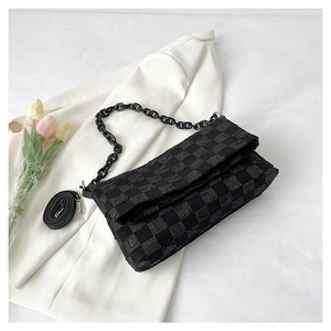 Detail of black checkered shoulder bag with chunky chain strap on a white blazer background