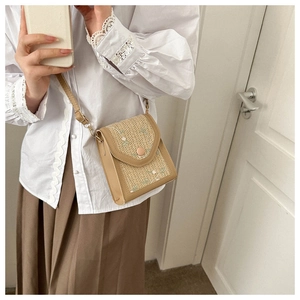 Detail view of woven straw crossbody bag with white flower embroidery and leather trim