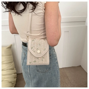 Detail shot of ivory woven crossbody bag featuring floral embroidery and round button