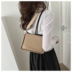 Detailed view of beige minimalist flap shoulder bag with wide leather strap on a model