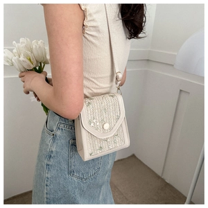 Detail of beige woven crossbody bag featuring green floral embroidery and round clasp