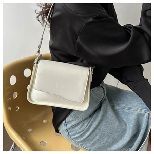 Close-up of cream rectangular leather shoulder bag with wide strap worn by model
