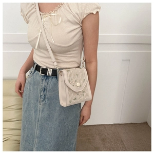 Detail of woven crossbody bag with green floral embroidery and flap closure
