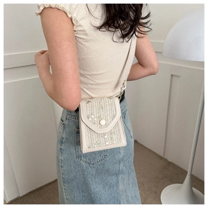 Close-up of off-white woven crossbody bag with floral embroidery and marble button detail