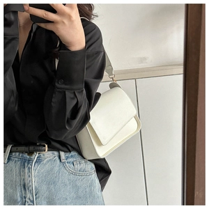 Detail of a minimalist white leather shoulder bag featuring gold metal hardware and flap