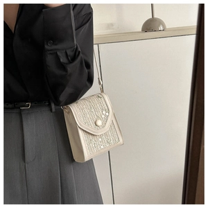 Straw shoulder bag with floral embroidery and pearl closure on a model with grey trousers