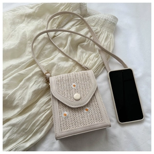Straw shoulder bag with daisy embroidery next to a phone for size comparison