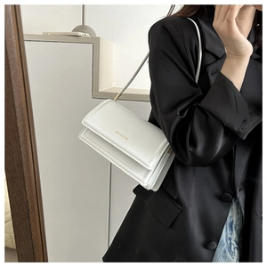 Close-up of white minimalist shoulder bag with gold logo and fine matte leather texture