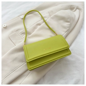 Detail of lime green leather shoulder bag with gold lettering on a chic cream blazer