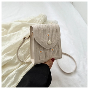Detail of beige straw crossbody bag featuring white daisy embroidery and gold metal buckle