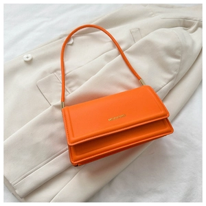 Close-up of vibrant orange leather shoulder bag with gold hardware on white blazer