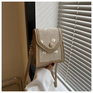 Detail of straw woven texture with white daisy embroidery and camel leather trim on phone bag