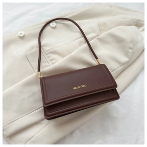 Close-up of dark brown leather shoulder bag with gold hardware on beige suit