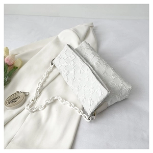 Detailed view of white quilted shoulder bag with plastic chain and bubble texture