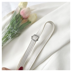 Close-up of white PU leather bag strap with silver metal buckle on white fabric